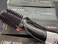View of one hot air brush resting on its box, showing brush head and handle, with cord coiled nearby.
