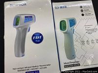 Photo of the packaging boxes for two infrared thermometers showing brand names, model (KZX-001), and features such as instant accuracy and fever alarm.