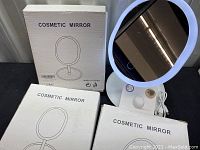Photo of two boxed cosmetic mirrors side by side with one mirror out of box showing white frame and base.