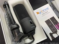 Microphone and tripod stand packed in a foam insert inside box, visible volume knob and packaging.