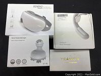 Four boxed massage tools from RENPHO, YEAMON, and unbranded including eye, scalp, neck massager, and facial massager set.