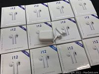 Boxed sets of i12 TWS wireless earphones with charging cases. Several packages and loose pairs arranged on black surface.