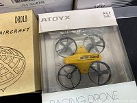 Yellow ATOYX Racing Drone in box with four propellers visible.