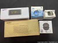 Five Bluetooth speakers in original packaging including Musky, Aukey, and Rokono brands arranged on a surface.