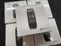 Lot of five KoreTrak smart watches in sealed white retail boxes, displayed in a group on a black surface.