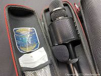 Open-box microphone in foam-lined carrying case with accessories and manual.