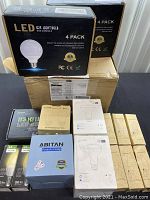 Multiple boxed packages of LED light bulbs including 4-pack G25 bulbs, smart WiFi bulbs, projector lamp box, and instruction manuals laid out on a box.