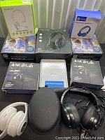 Lot contents showing boxed headphones from AUSDOM, Phonix, iClever, Ikela, call center headset box, and two loose headphone sets with headphone case in front.