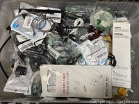 Top view of mixed cables and accessories in storage bin; includes USB data cables in boxes and smaller packaged accessories