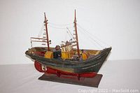 Full view of the hand-crafted ship model showing dark green hull with red bottom and mounted on a wooden stand.