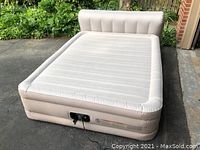 Inflated air mattress with attached headboard shown on driveway, powered by 115V electric plug on front panel