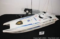 White twin hull radio controlled speed boat with blue and grey decals, parked on black background with remote control visible