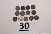 Top-down view of 13 Indian Head Pennies arranged in three rows with auction lot number sign 30