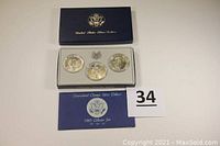Opened display box showing three uncirculated silver dollars in protective capsules inside the presentation box, along with an information booklet.