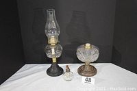 Three vintage kerosene oil lamps displayed against a black background, showing overall condition and size difference.