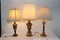 Photo showing three solid brass lamps with shades, all lit, on a white background, displaying their varying styles and sizes.