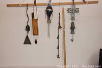 Five wind chimes and bells hanging on a wooden rack with a yardstick for size reference.