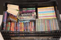 Photo showing a black plastic crate filled with books arranged in sets and stacks, illustrating the quantity and condition of the collection.