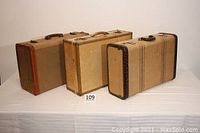 Three vintage tweed and tan suitcases displayed side by side showing various sizes and wear levels.