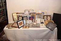 Wide view of the collection of frames on a table, showing multiple frames of differing sizes and shapes, upright and stacked.