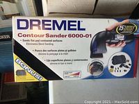 Photo of the product box showing Dremel logo, product name Contour Sander 6000-01 and highlighting features like sanding flat and contoured surfaces and faster speed.
