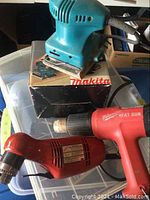 Milwaukee heat gun, Milwaukee drill, and Makita sander with box.