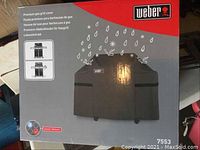 Photo of Weber BBQ cover in box showing front packaging with product image and branding.