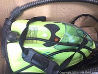 Close-up of the green and black steamer device showing hose, handle, and some cables.