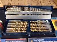 Open box of Mastercraft drill bits organized by size, gold-colored, in a blue metal case.