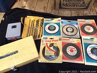 Photo showing drill bits in yellow case, gray plastic box, wooden Mastercraft box, and cutting discs in packaging