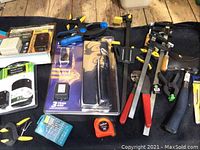 Image showing cordless cutters in packaging, clamps, drill bit set, tape measure, and other hand tools spread on black cloth.