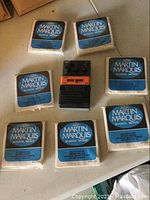 Photo showing seven packs of Martin Marquis acoustic bronze guitar strings arranged around an Arion Overdrive pedal on a flat surface.