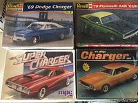 Four model car kits in original boxes depicting Dodge and Plymouth classic muscle cars, including '69 Dodge Charger, '70 Plymouth AAR 'Cuda, Super Charger by MPC, and '69 Dodge Charger 500.