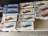 Photo from an overhead angle showing 10 boxes of plastic display cases for 1:25 scale model cars from AMT, Jo-Han, Sho Case, and IMEX, with visible wear and dust on boxes.
