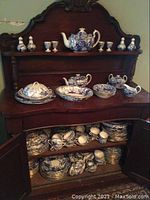 Wooden hutch top shelf and surface holding a large teapot, egg cups, salt and pepper shakers, covered and open serving dishes