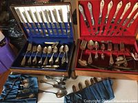 Two wooden cases, one with red and one with blue interiors, holding silver plated flatware including knives, forks, and spoons. Additional loose utensils in blue fabric pouch.