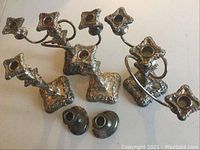 Wide view showing the multi-arm candelabra and tall single candle holder with ornate square bases, featuring floral and scroll decorative patterns.