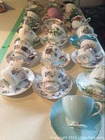 Overview of twelve teacup and saucer pairs on counter