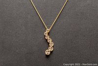 Close-up of gold chain necklace with pendant showing front side with seven bezel-set round stones.