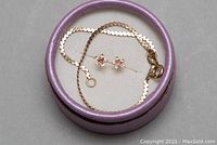Pair of 14kt gold floral earrings with pink and clear stones along with 10kt gold chain bracelet coiled together in a round purple container.