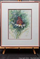 Framed watercolour painting of butterfly on a daisy flower showing overall view on easel.