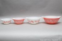 Four Pyrex Gooseberry pink mixing bowls arranged side by side from smallest to largest