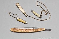 Photo showing all three blades, the large carved straight razor folded and the two smaller pocket blades attached to chains, displayed on neutral background.