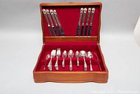 Full view of wooden chest open showing knives secured in lid and remaining flatware in base.