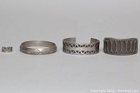 Four pewter jewelry pieces arranged side by side: small ring, two open cuff bangles, one closed cuff bangle, all with geometric design elements.