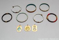 Photo shows seven colorful cloisonné bangles arranged with three cloisonné pendants below them, on a grey flat surface.