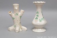 Two Belleek bud vases, one shaped like a tree trunk with three openings, and the other a traditional vase with a ruffled rim, both decorated with shamrocks and gold accents.