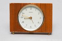 Front view of Birks wind-up alarm clock showing wooden rectangular case and round white dial with black numerals and gold hands.