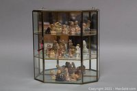 Handmade brass and glass wall cabinet displaying 19 Wade figurines arranged on three shelves, with a front glass door closed.