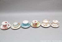 Full view of all 12 teacups with matching saucers arranged in a row showing various flower patterns and colors